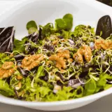A fresh salad with mixed greens, sprouts, red onion, and walnuts in a white bowl.
