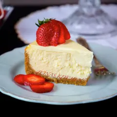En bit krämig cheesecake med jordgubbar på en ljusblå tallrik. Undrar du hur länge håller cheesecake i kylen? Denna ser god ut!
