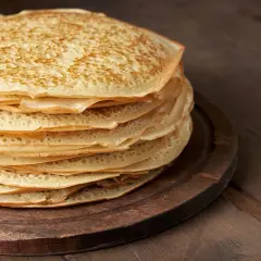 En hög med gyllene pannkakor, perfekt för ett gott pannkakssmet recept. De ligger på en mörk träskärbräda.