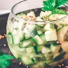 En glasburk fylld med tärnad gurka, senapsfrön och en kvist persilja. Ett enkelt gurksallad recept.