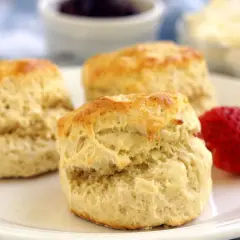 Tre gyllene scones på en vit tallrik, redo att avnjutas med sylt och grädde. Ett perfekt scones recept för fikat.