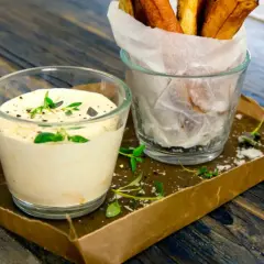 En krämig sås med creme fraiche, toppad med örter, bredvid ett glas med krispiga pommes frites.