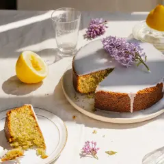 En saftig kaka med citron och vallmofrön, täckt med glasyr och dekorerad med syren. En bit är upplagd på en tallrik med en gaffel.