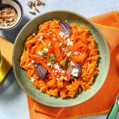 En skål med orzo pasta med rostade grönsaker och fetaost, perfekt för medelhavskost recept. Toppad med mandlar och färska örter.