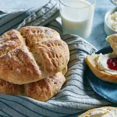 Nybakade scones med sylt och grädde, serverade med ett glas mjölk. Perfekt för en mysig fika.