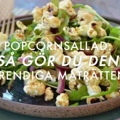 A close-up of a popcorn salad with greens and red onion on a dark plate, with a fork.