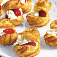 Cream puffs filled with whipped cream and topped with raspberries and strawberries on a white platter.