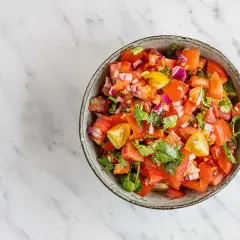 En skål med färsk pico de gallo, full av hackade tomater, rödlök och koriander, redo att serveras.