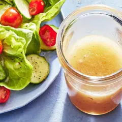 En burk med gyllene dressing till sallad står bredvid en fräsch sallad med gurka och tomater.