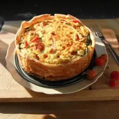 En gyllene tacopaj utan pajdeg, fylld med ost, tomater och spenat, serveras på en träskärbräda.