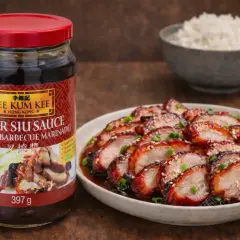 En burk Lee Kum Kee Char Siu Sauce, en kinesisk bbq sås, bredvid en tallrik med skivat, glaserat fläskkött och en skål ris.
