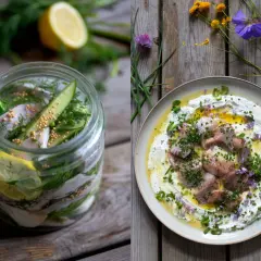 Inlagd sill i burk med dill, citron och gurka. Sill på en bädd av gräddfil med gräslök och blommor. Klassisk midsommar mat.