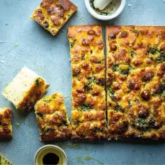 En gyllene focaccia långpanna med örter och flingsalt, uppskuren och redo att avnjutas.