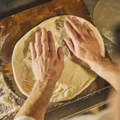 Händer formar pizzadeg på en skärbräda med mjöl. Ett steg i ett klassiskt pizza recept.