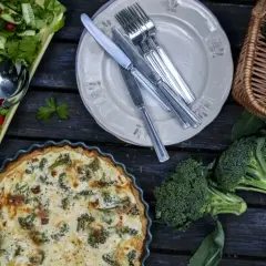 En gyllene västerbottenpaj med broccoli, en fräsch sallad och färsk broccoli i en korg. En härlig måltid!
