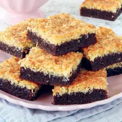 En hög med kladdkaka med kokostosca på en rosa tallrik. Den mörka chokladkakan toppas med en gyllene, krispig kokosbädd.