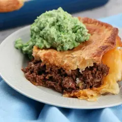 En bit köttfärspaj utan äggstanning med en klick grön mos på en tallrik.