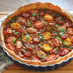 En gyllene köttfärspaj med körsbärstomater och färska örter, redo att serveras.