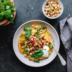 En skål med en gyllene gryta toppad med kikärtor, bär och spenat. Perfekt för vegetariska recept.