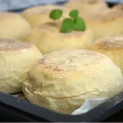 En bricka med nybakade, gyllene english muffins, redo att delas och njutas. En liten grön kvist vilar på en av dem.