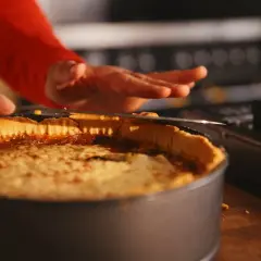 En person skär en gyllene quiche lorraine i en form. Den ser utsökt ut!