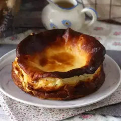En krämig baskisk cheesecake med karamelliserad yta, serverad på en tallrik med blommig duk.