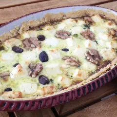 Spinach and feta quiche with walnuts and olives in a rustic tart dish.