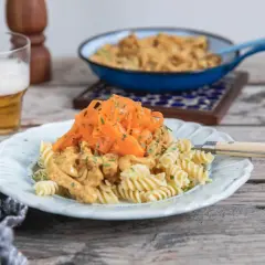 En tallrik med rotfrukter och ost och skinksås över pasta. En öl står bredvid.