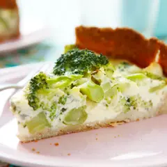En bit broccoli och ädelostpaj på en rosa tallrik. Pajen har en gyllene botten och fyllning med broccoli och krämig ost.