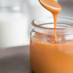 En sked häller krämig kolasås i en glasburk. Perfekt för ditt kolasås recept!