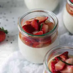 Pannacotta in glass jars topped with fresh strawberries and rosemary.