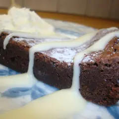 En saftig kladdkaka med sirap, pudrad med florsocker och toppad med vispad grädde.
