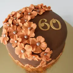 Chokladtårta med aprikosfärgade blommor och guldigt "60" som firar en 60-årig födelsedag.
