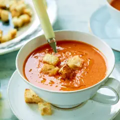 En skål med gazpacho, toppad med krutonger. Bredvid en karaff med olivolja. Ett perfekt gazpacho recept för en varm dag.
