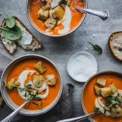 Tre skålar med krämig tomatsoppa, gjord på krossade tomater, toppas med krutonger och en virvel av grädde. Serveras med gott bröd och färsk spenat.