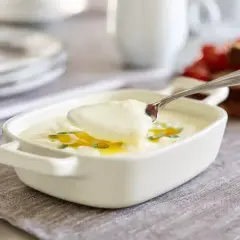 En sked lyfter krämig bechamelsås ur en vit skål, garnerad med gräslök och olja. Perfekt för ditt bechamelsås recept.