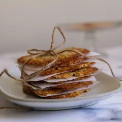 Stack of thin, golden-brown oat cookies tied with twine on a white plate.