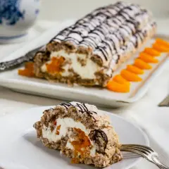 En bit av en läcker budapest bakelse med aprikoser och grädde, dekorerad med choklad och pudersocker.