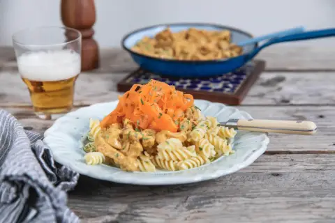 En tallrik med rotfrukter och ost och skinksås över pasta. En öl står bredvid.