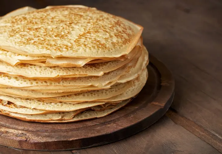 En hög med gyllene pannkakor, perfekt för ett gott pannkakssmet recept. De ligger på en mörk träskärbräda.