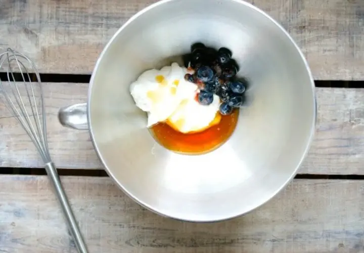 En skål med yoghurt, honung och blåbär, redo att vispas till en härlig frozen yoghurt. En visp ligger bredvid.