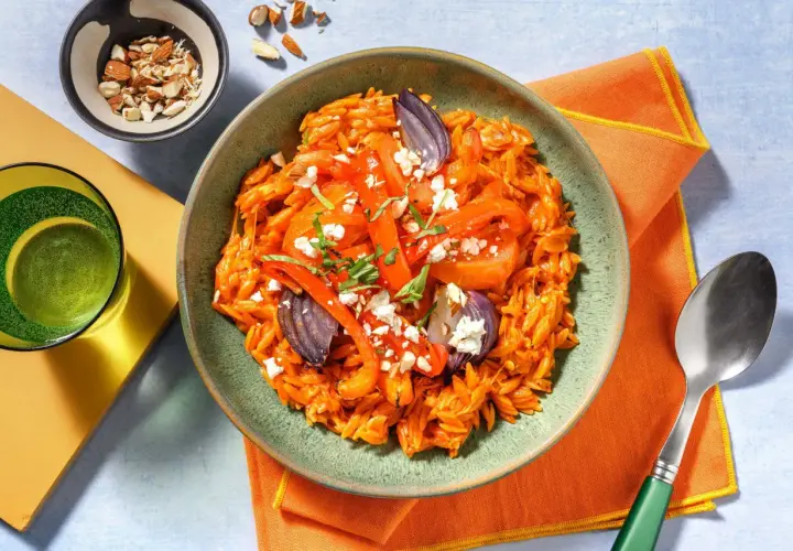 En skål med orzo pasta med rostade grönsaker och fetaost, perfekt för medelhavskost recept. Toppad med mandlar och färska örter.