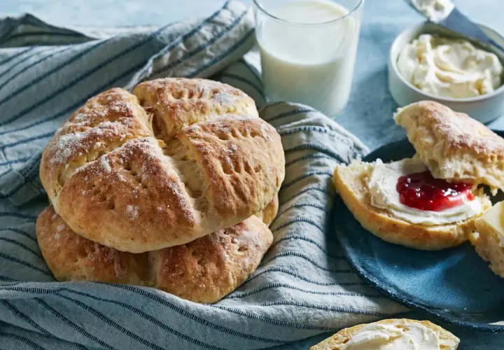 Nybakade scones med sylt och grädde, serverade med ett glas mjölk. Perfekt för en mysig fika.