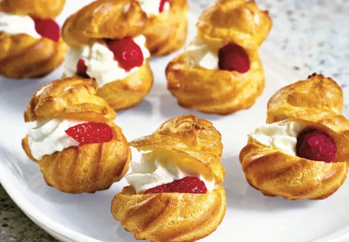 Cream puffs filled with whipped cream and topped with raspberries and strawberries on a white platter.