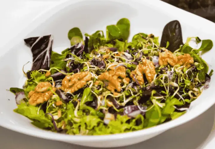 A fresh salad with mixed greens, sprouts, red onion, and walnuts in a white bowl.