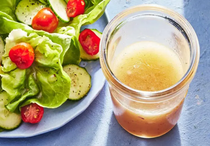 En burk med gyllene dressing till sallad står bredvid en fräsch sallad med gurka och tomater.