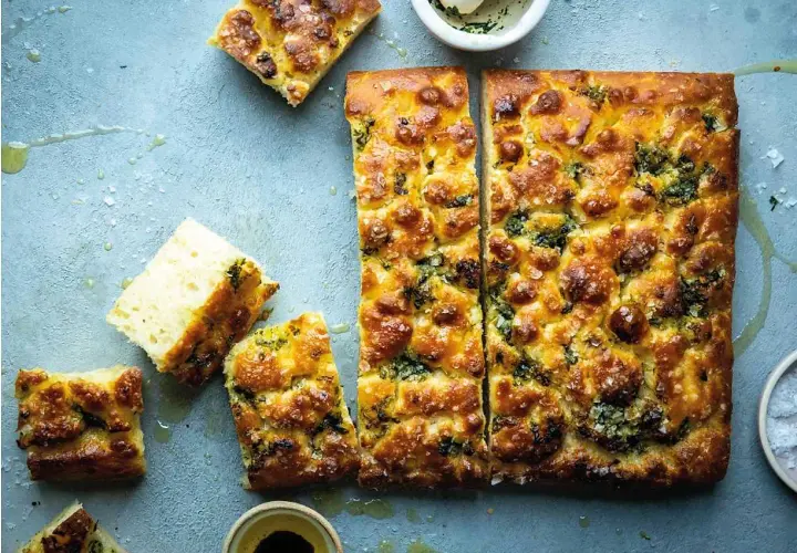 En gyllene focaccia långpanna med örter och flingsalt, uppskuren och redo att avnjutas.