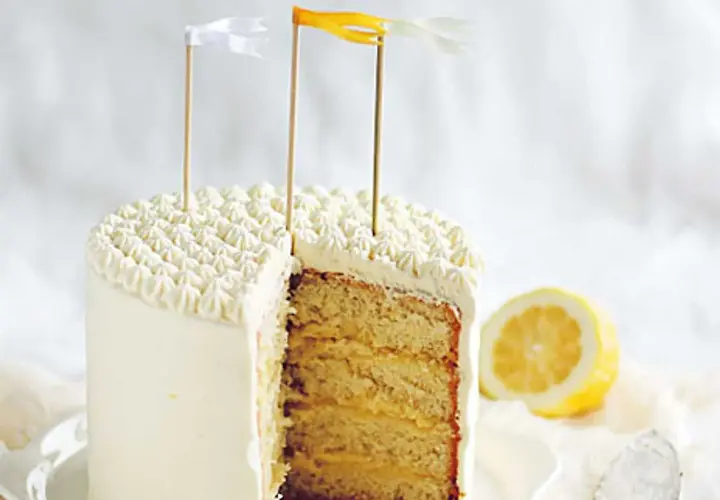 Tårta med fluffig frosting och lager av saftig sockerkaka fylld med syrlig lemon curd. En citronskiva ligger bredvid.