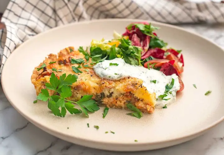 En bit saftig skinkpaj utan ost, toppad med färska örter och en klick krämig sås, serveras med en fräsch sallad.