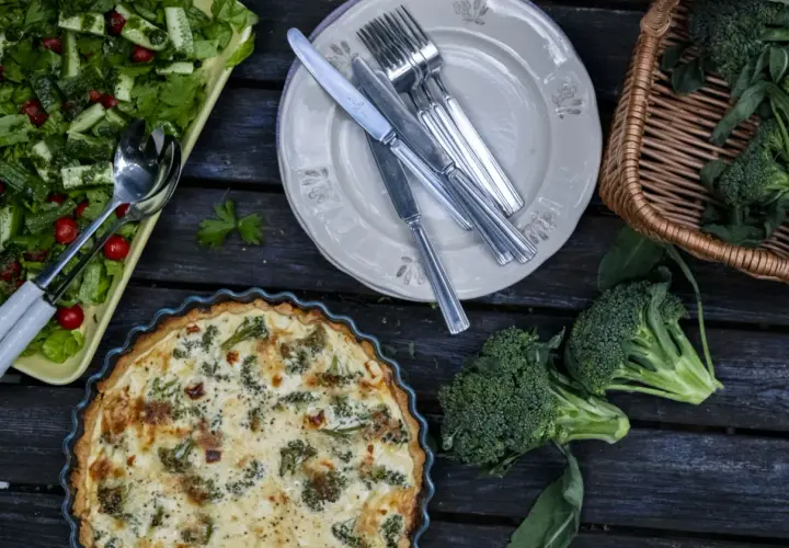 En gyllene västerbottenpaj med broccoli, en fräsch sallad och färsk broccoli i en korg. En härlig måltid!